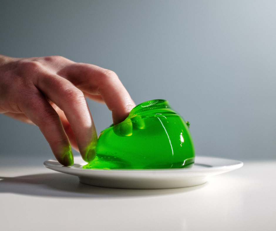 Hand touching green jelly on plate.