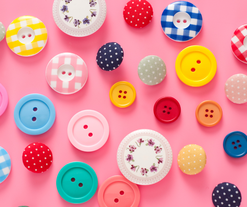 Assorted colorful sewing buttons on pink background.