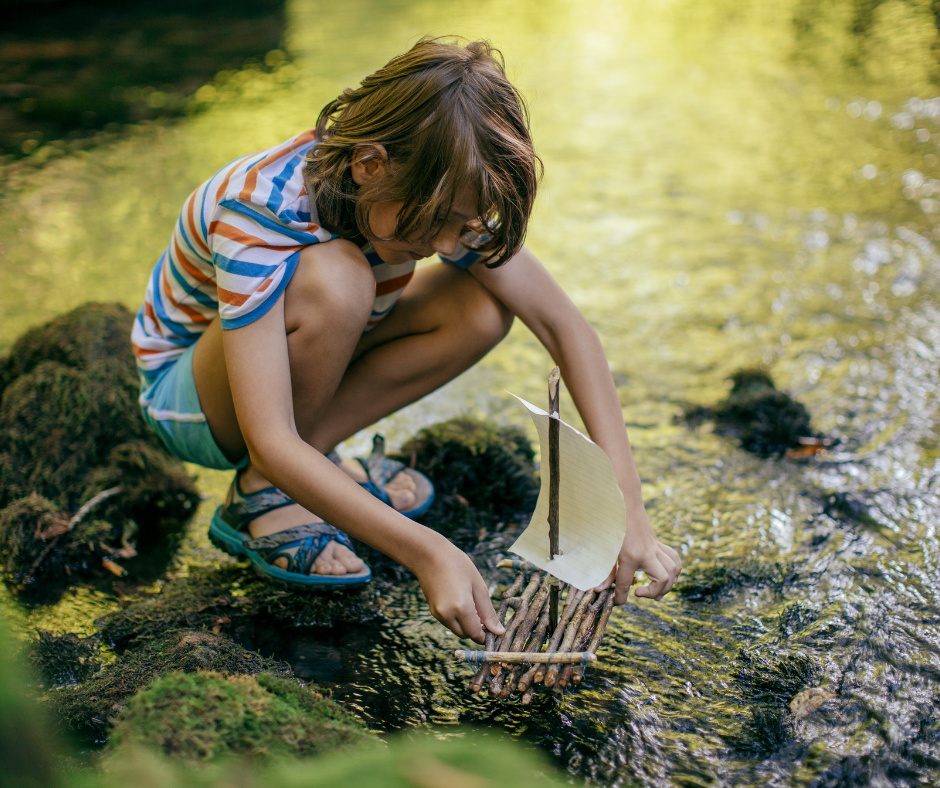 Child playing with handmade boat by stream