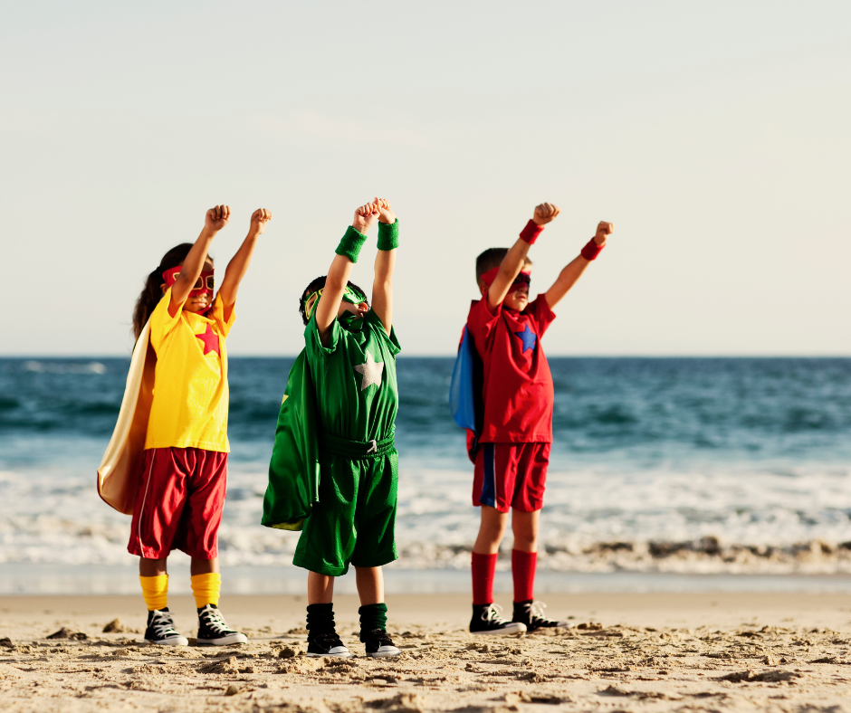 Children in superhero costumes playing on beach
