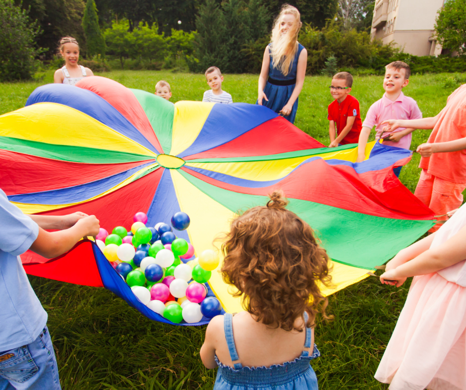 Children playing with colorful parachute and balls outdoors.