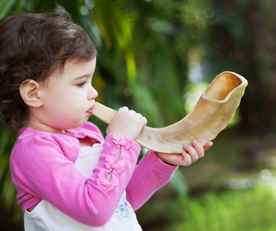 Child blowing a shofar horn outdoors.