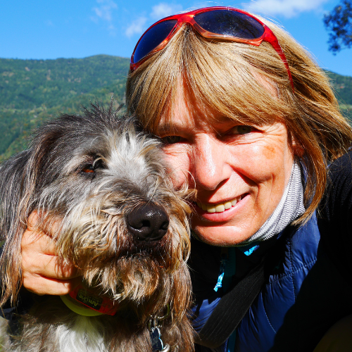Woman smiling with scruffy grey dog outdoors.
